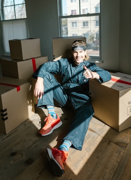 a packers and movers employee sitting in in the middle of boxes and showing thumbs up